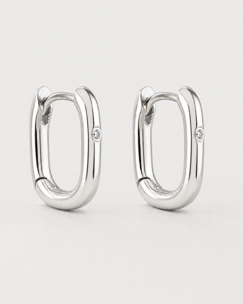 Pair of Clea sterling-silver single-crystal huggies on a seamless pale dove-grey background