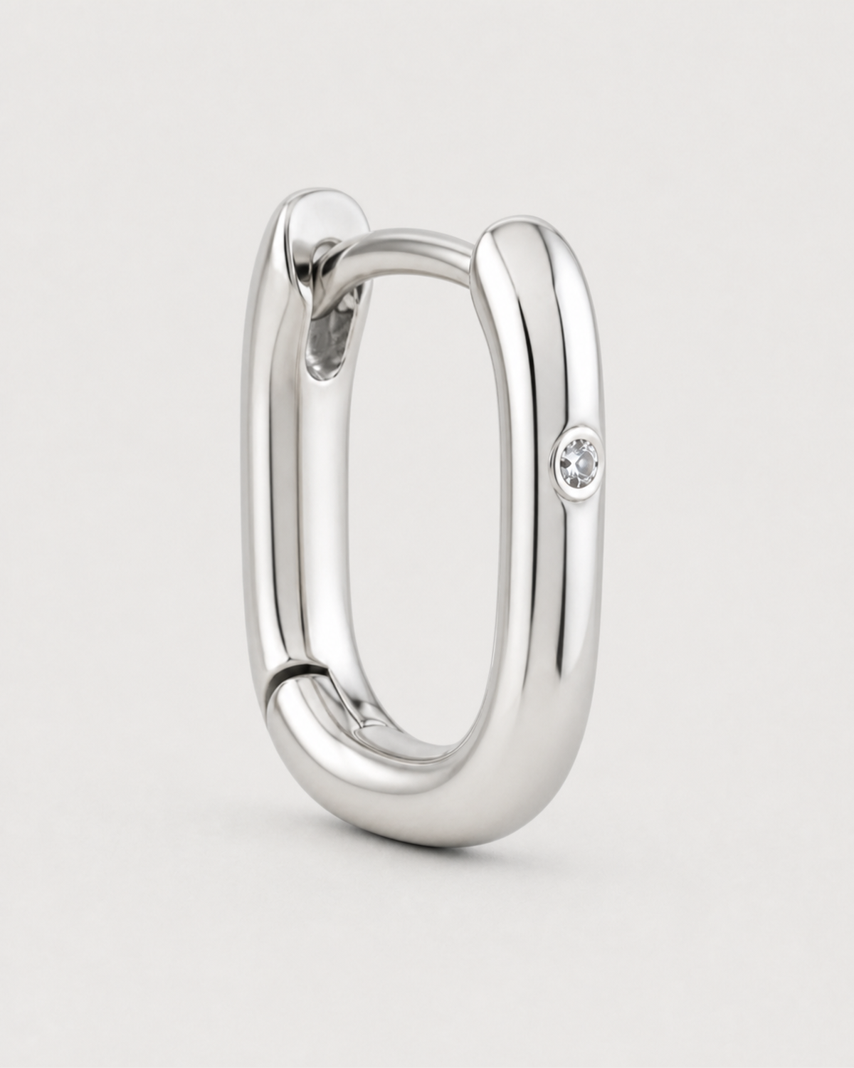 Macro detail of one polished Clea silver huggie with a single flush-set clear crystal