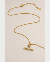 Delphine gold-tone toggle necklace in an alternate curved arrangement on pale grey