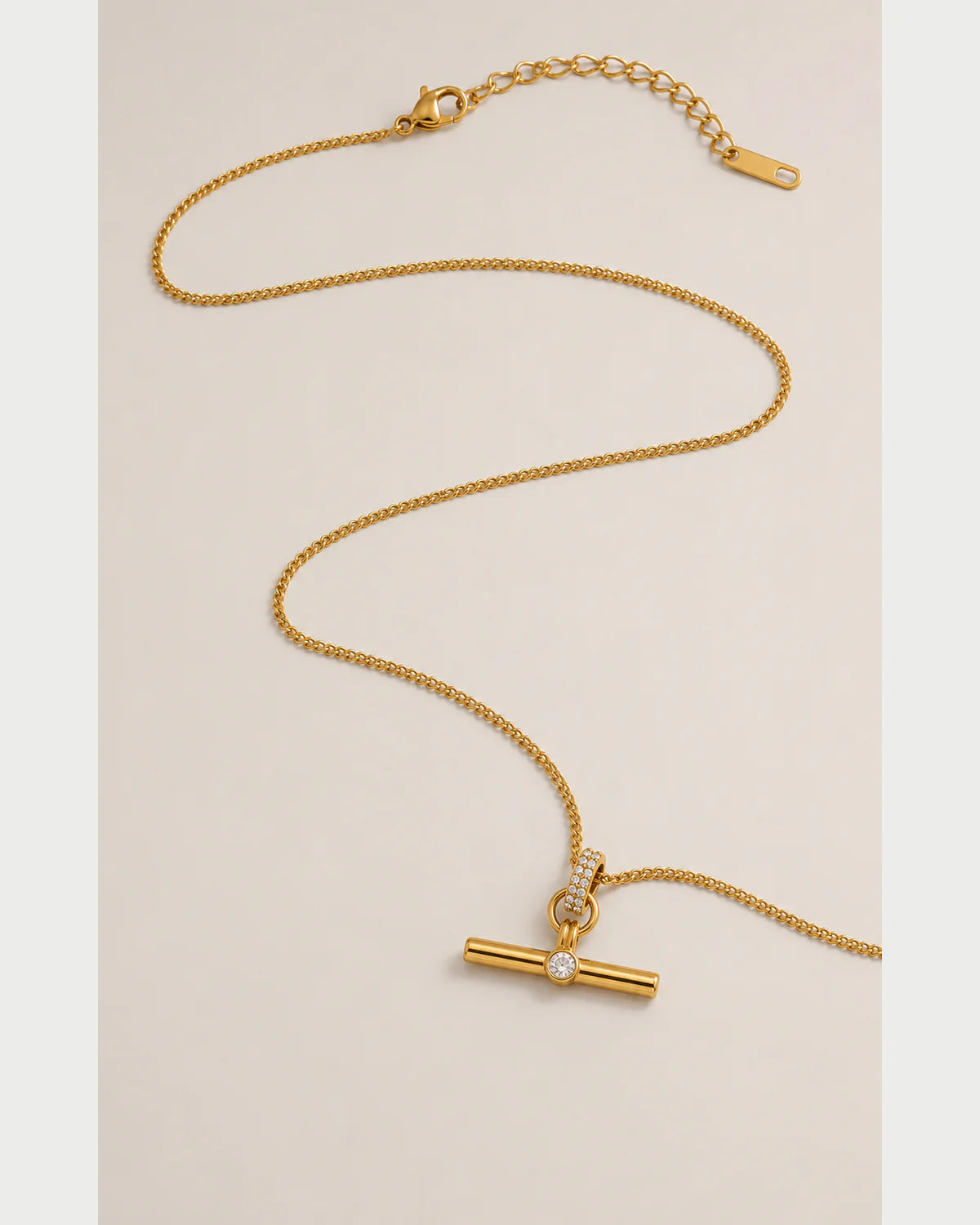Delphine gold-tone toggle necklace in an alternate curved arrangement on pale grey