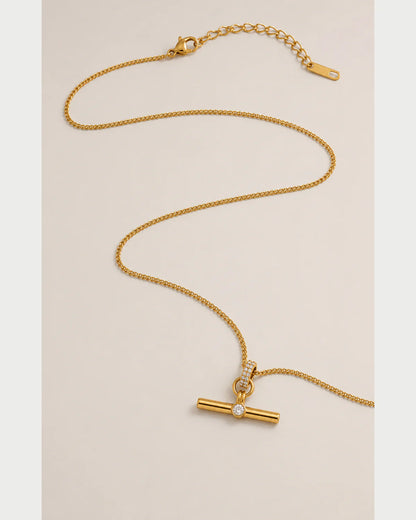 Delphine gold-tone toggle necklace in an alternate curved arrangement on pale grey