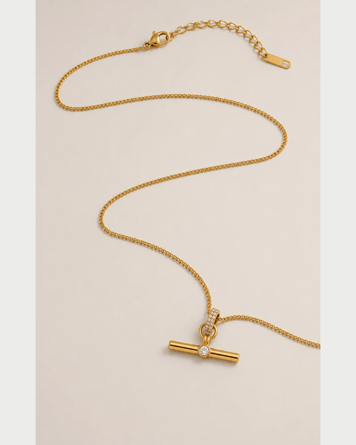Delphine gold-tone toggle necklace in an alternate curved arrangement on seamless pale grey