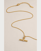 Delphine gold-tone toggle necklace in an alternate curved arrangement on seamless pale grey