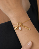 Extreme wrist macro of the Elara mama charm, gold heart and white pearl