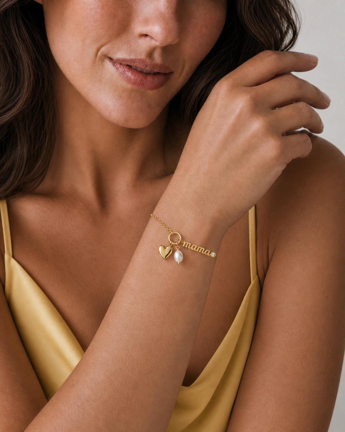 Close wrist view of the Elara mama, heart and pearl charms with butter-yellow silk