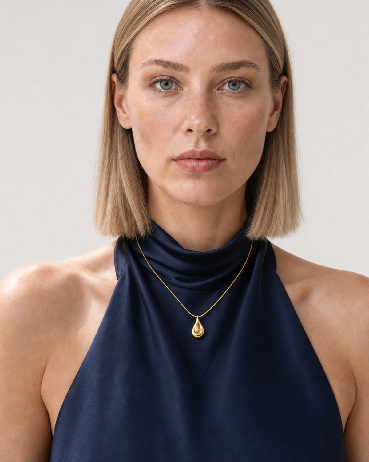 UK model aged 25 to 28 wearing the Elara gold droplet necklace in a pale dove-grey studio