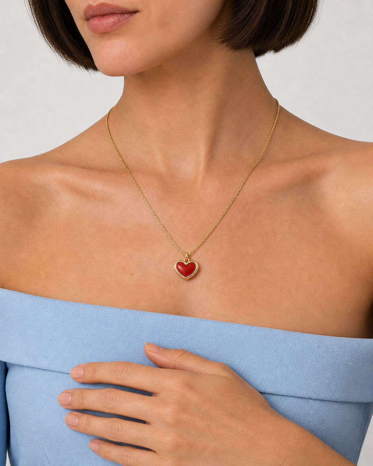 Alternate worn detail of the Estelle red enamel heart necklace with a relaxed hand below