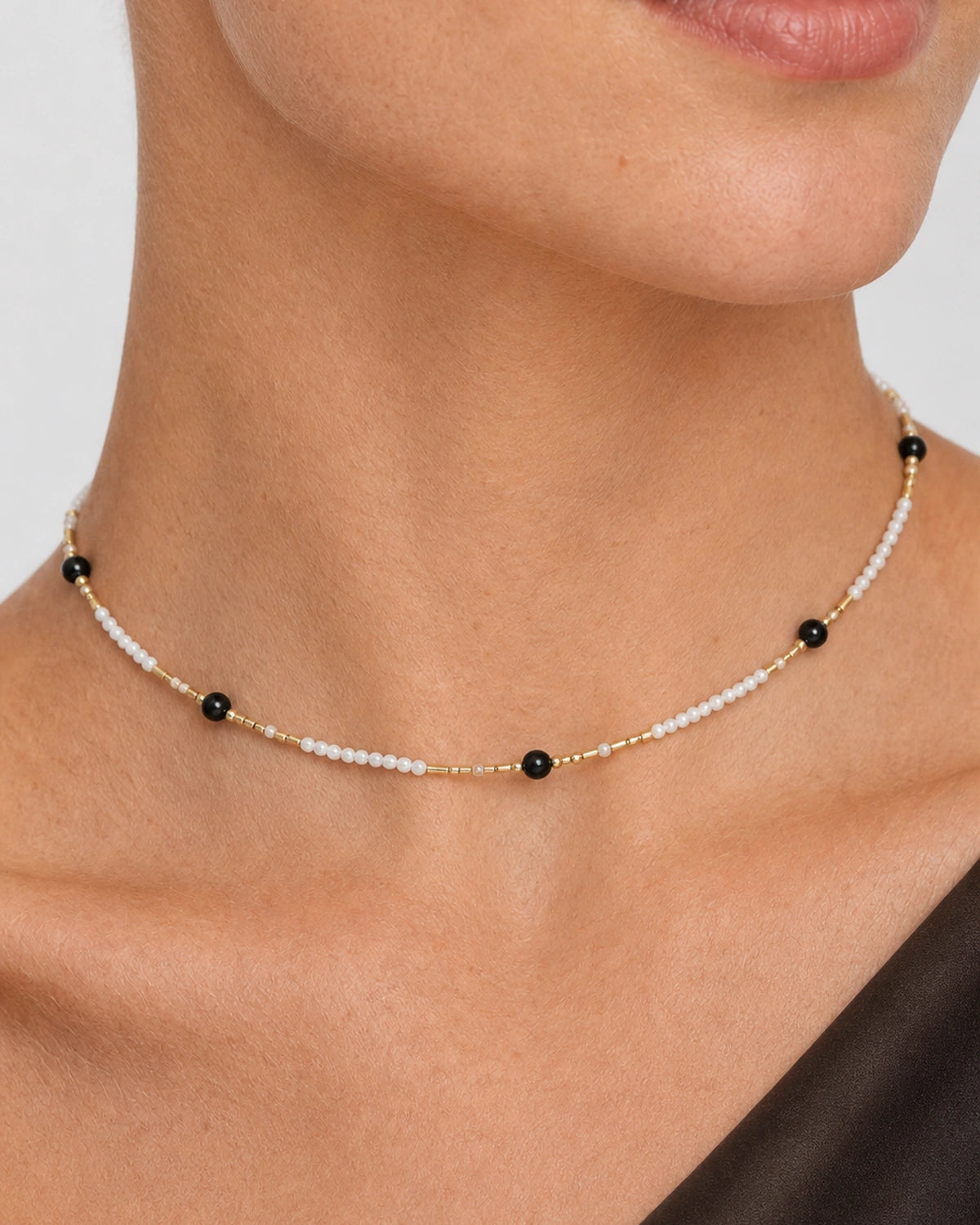 Extreme on-body macro of Isla seed beads, black accents and gold tube spacers
