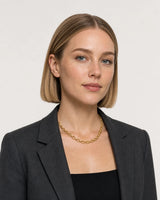 Model in charcoal tailoring wearing the Liora orbit chain in a pale dove-grey studio