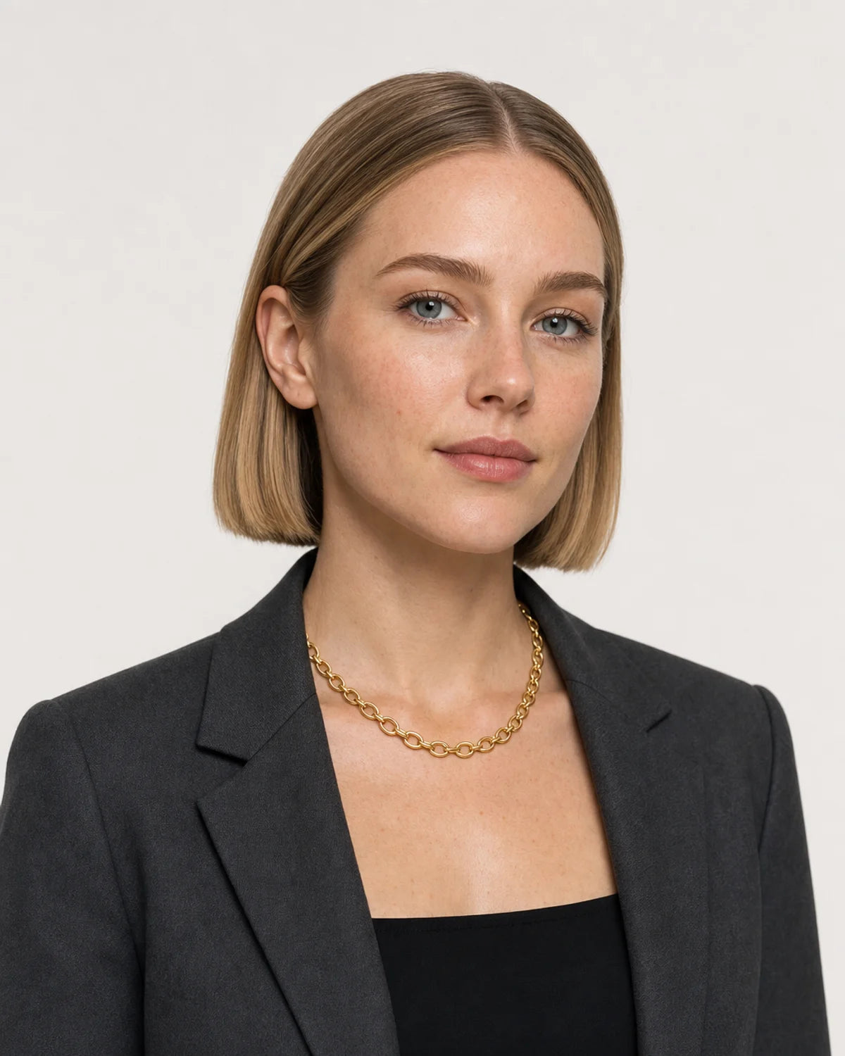 Model in charcoal tailoring wearing the Liora orbit chain in a pale dove-grey studio