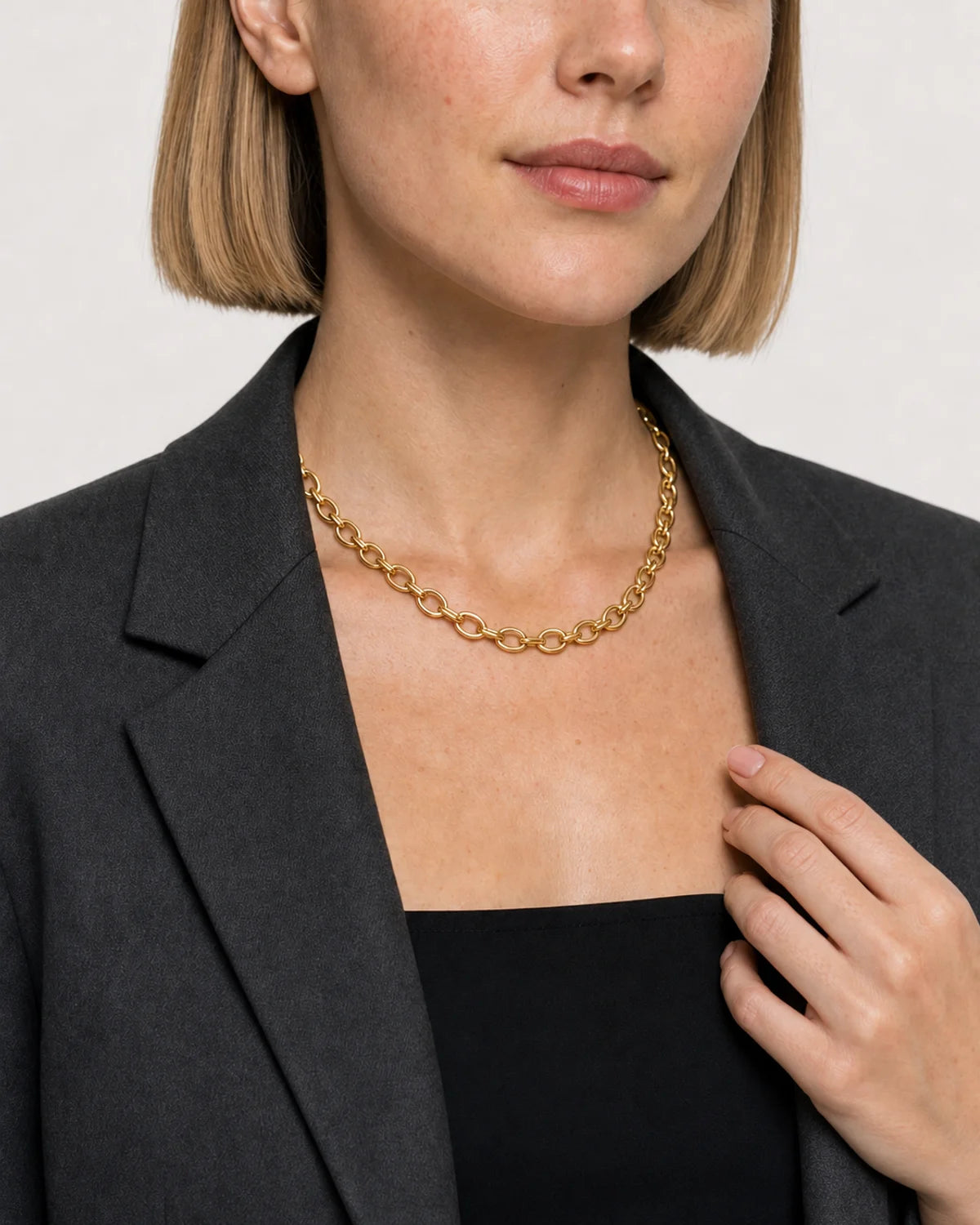 Human-scale wearing detail of the Liora chain beside charcoal tailoring