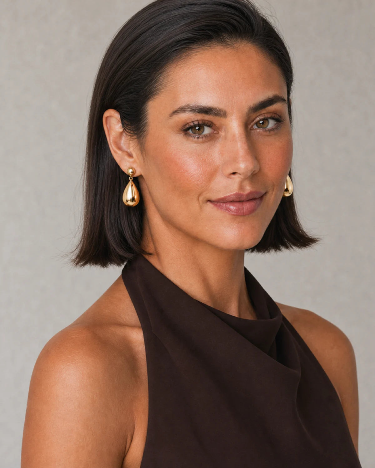 Three-quarter model portrait wearing Luma gold teardrop earrings with a warm side smile