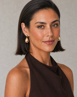 Three-quarter model portrait wearing Luma gold teardrop earrings with a warm side smile