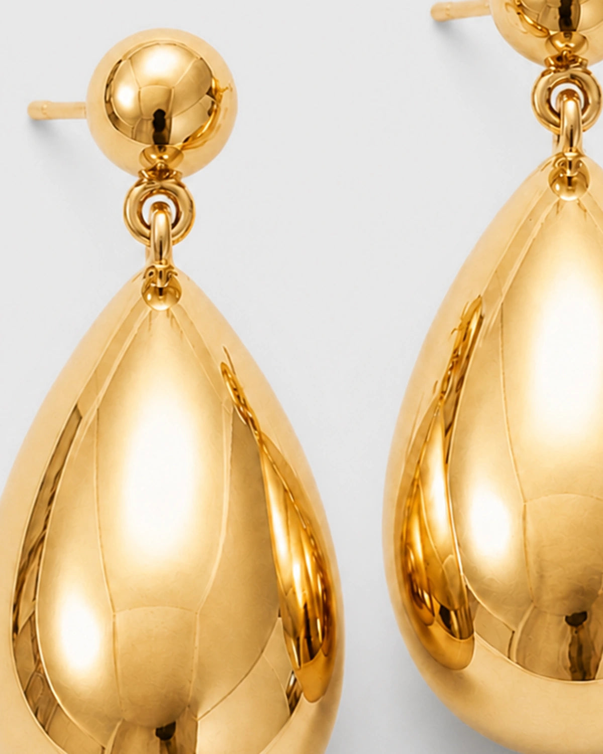 Macro view of Luma gold spherical studs and sculptural teardrops on travertine