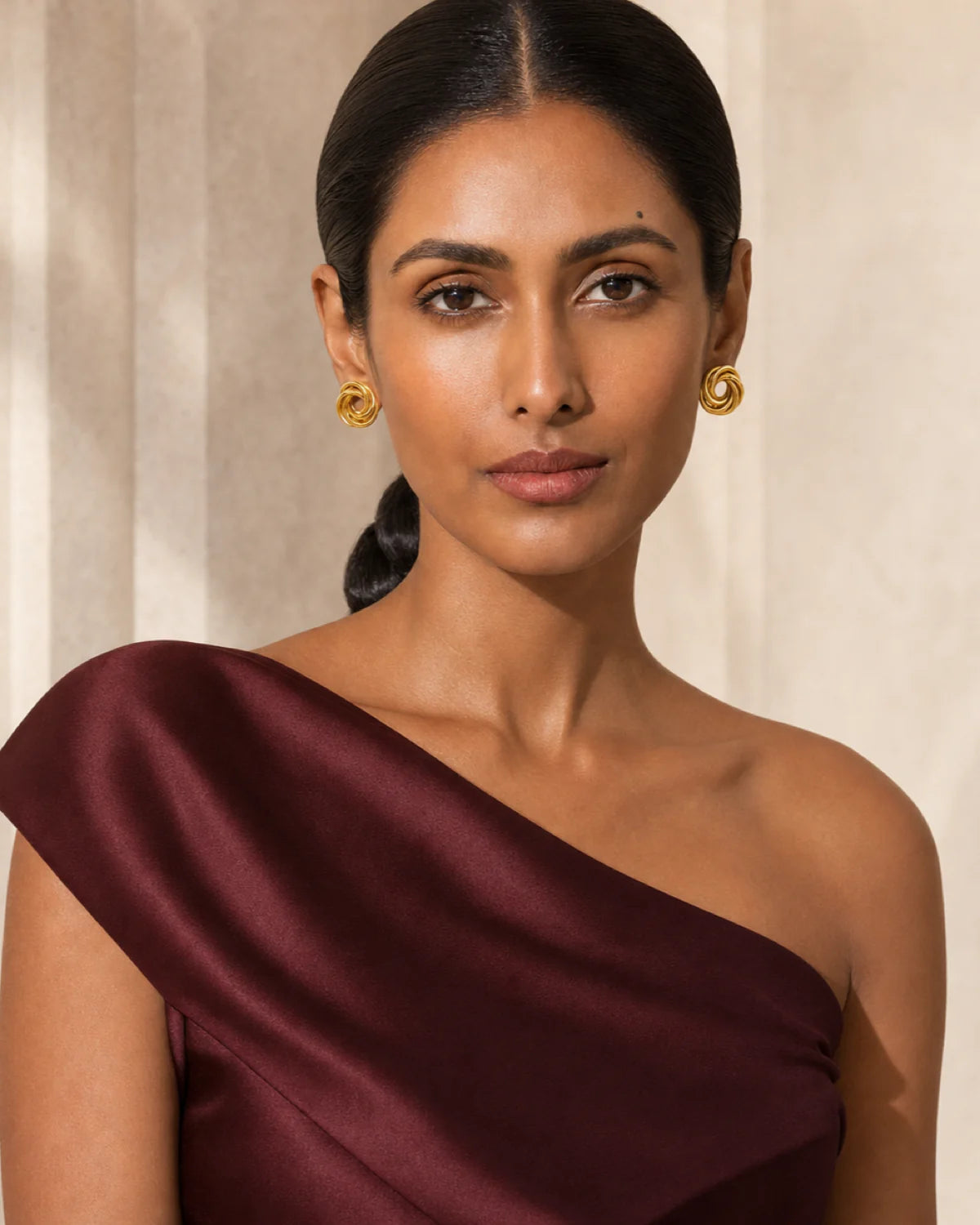 Model in garnet satin wearing Lyra circle knot studs with a direct gaze