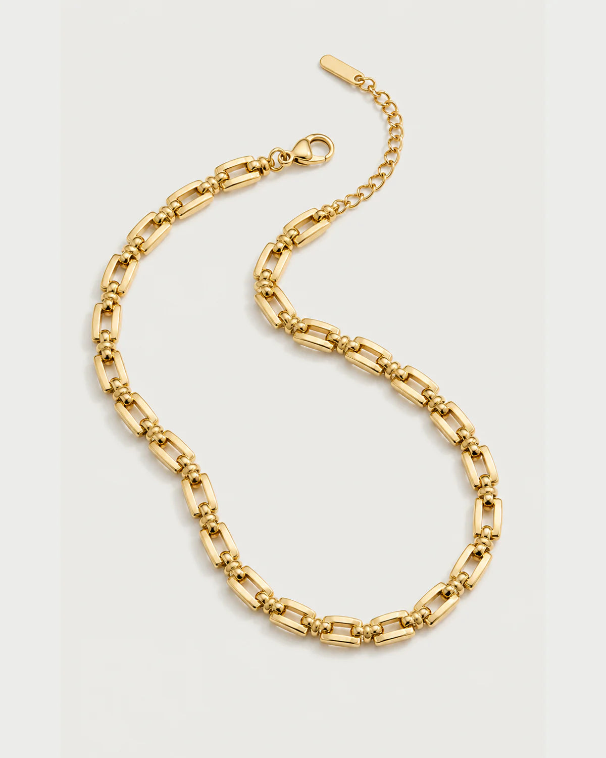 Marcelle gold-tone link necklace in an alternate curved arrangement on pale grey
