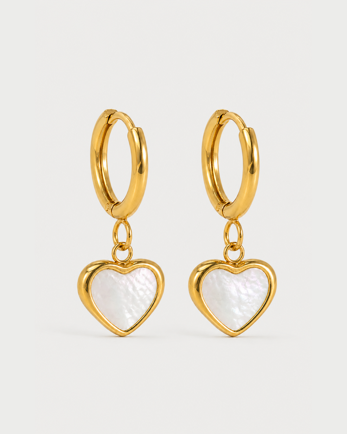 Pair of Maris gold mother-of-pearl heart huggies on a seamless pale dove-grey background