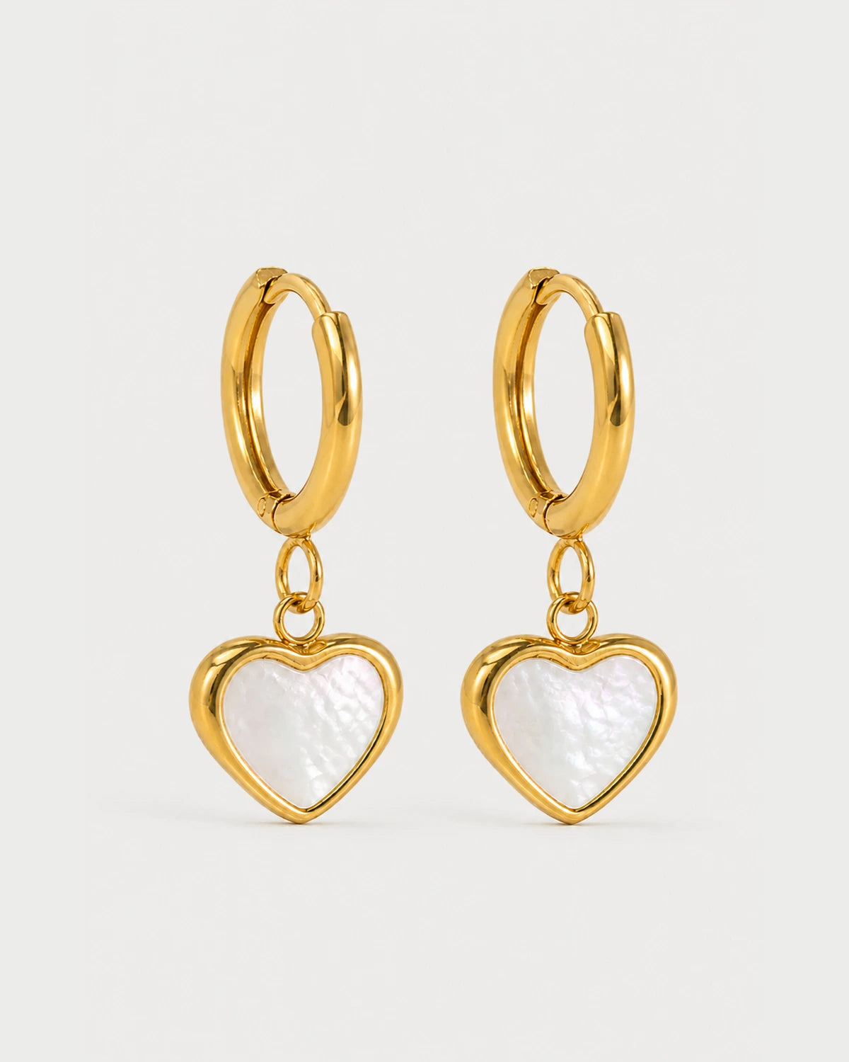 Pair of Maris gold mother-of-pearl heart huggies on a pale neutral-grey studio background