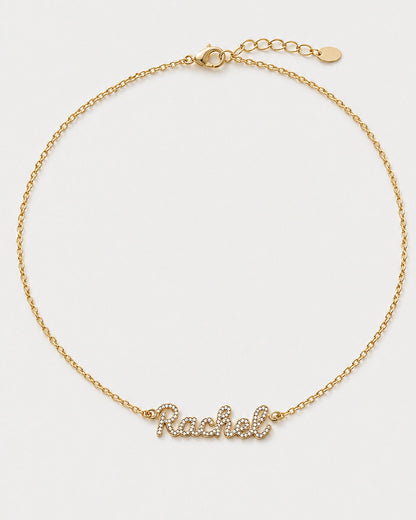 Mira gold pavé Rachel name necklace with round clasp, extender and oval tag on pale neutral grey