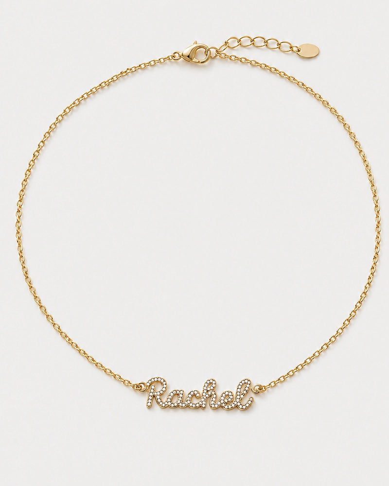 Mira gold pavé Rachel name necklace with round clasp, extender and oval tag on pale neutral grey