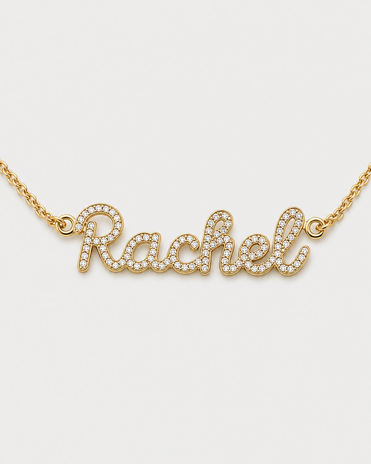 Macro view of the gold Mira connected cursive Rachel nameplate and clear pavé