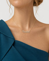 Mouth-down studio portrait wearing the gold Mira Rachel necklace with a petrol-teal silk top