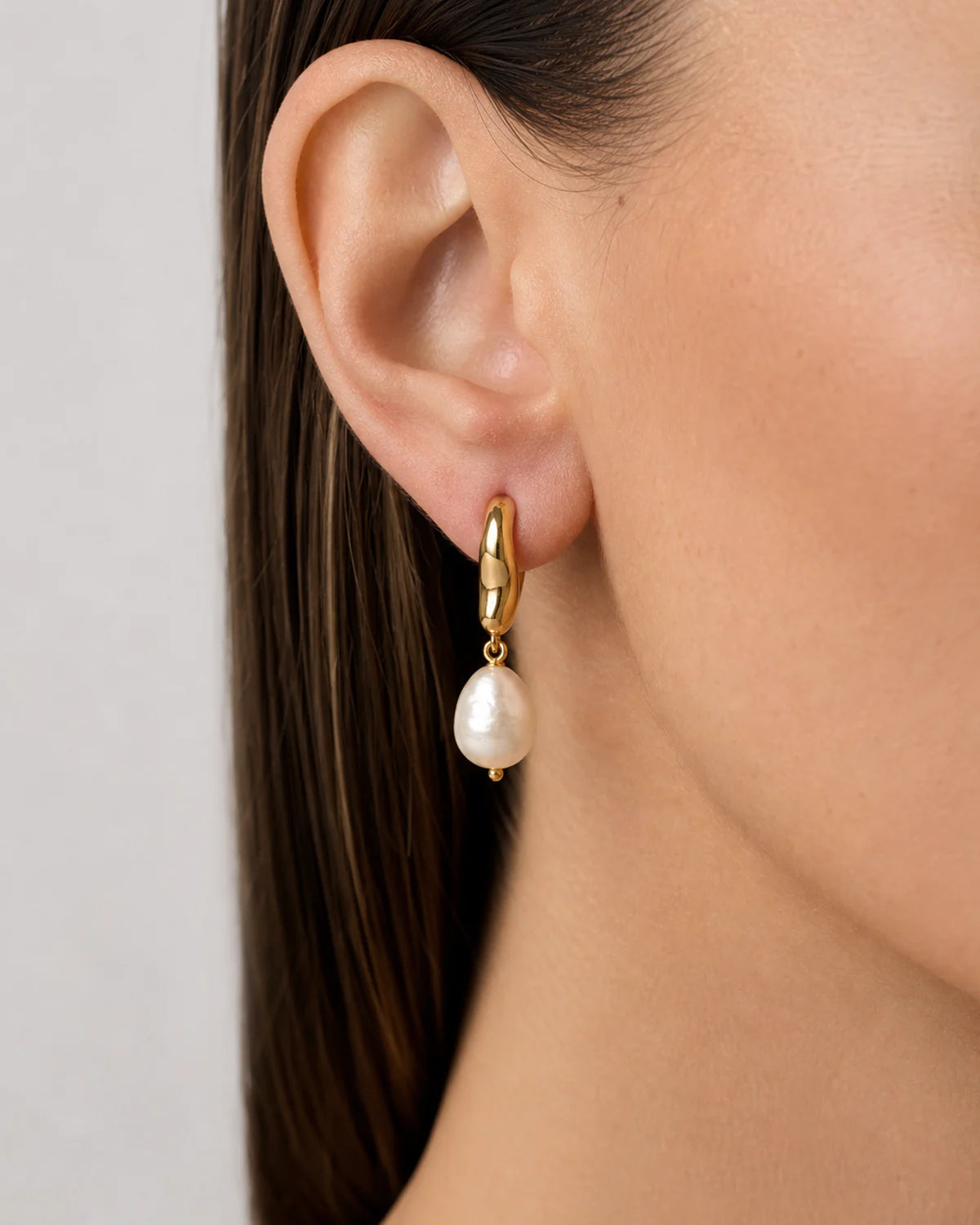 Extreme ear macro of Mirelle gold huggie and organic pearl