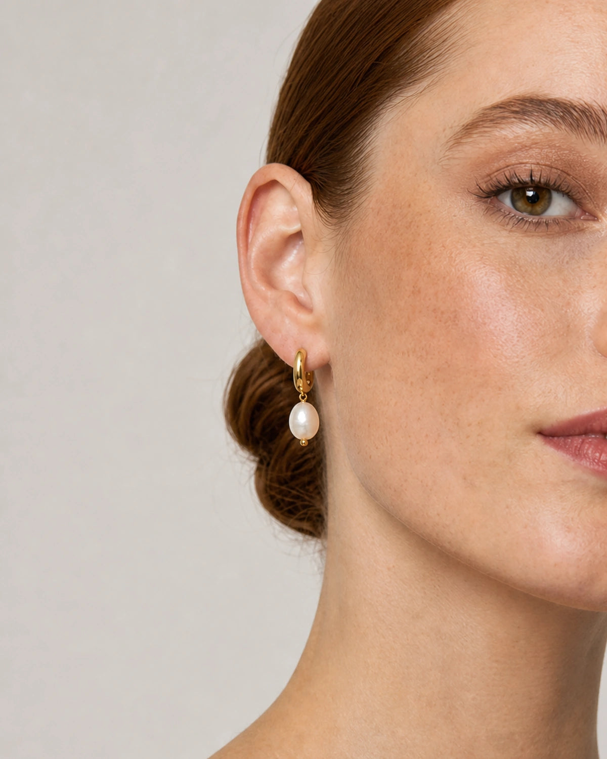Close on-ear view of the Mirelle gold huggie and organic ivory pearl
