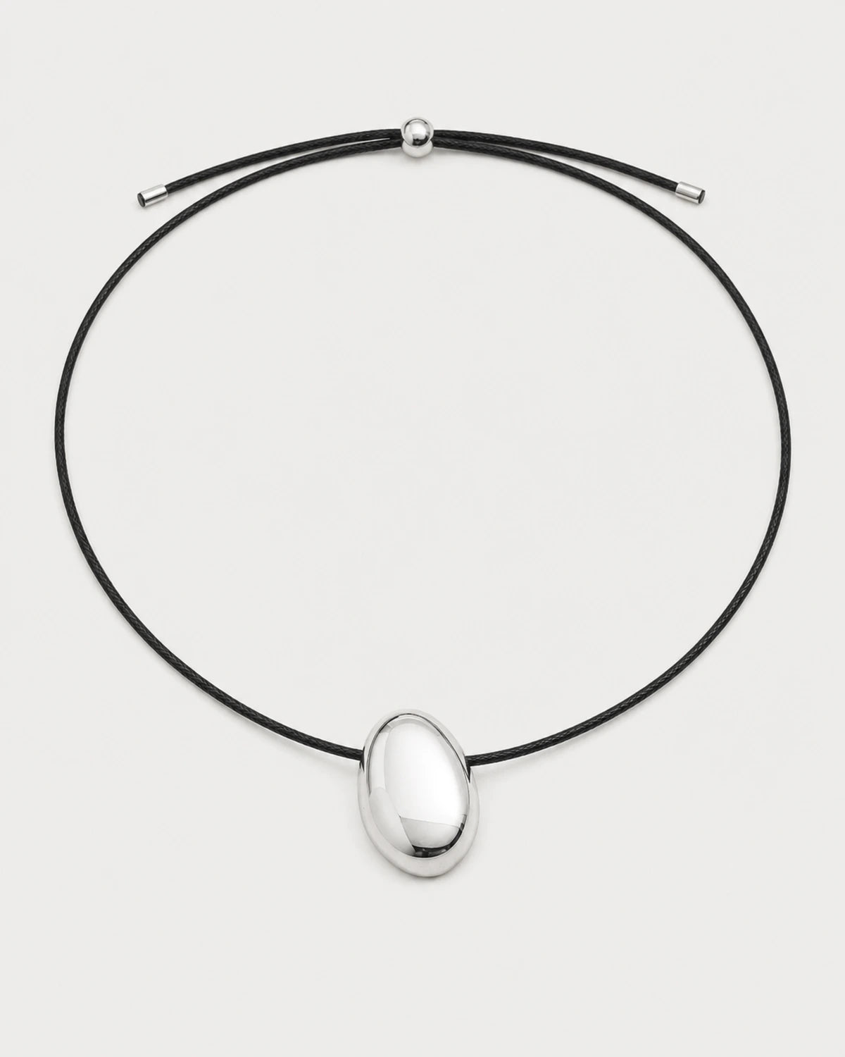 Naiya silver pebble cord necklace on a pale neutral-grey studio background