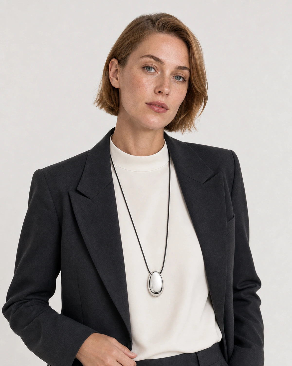 Human-scale studio view of the Naiya silver cord necklace with black tailoring