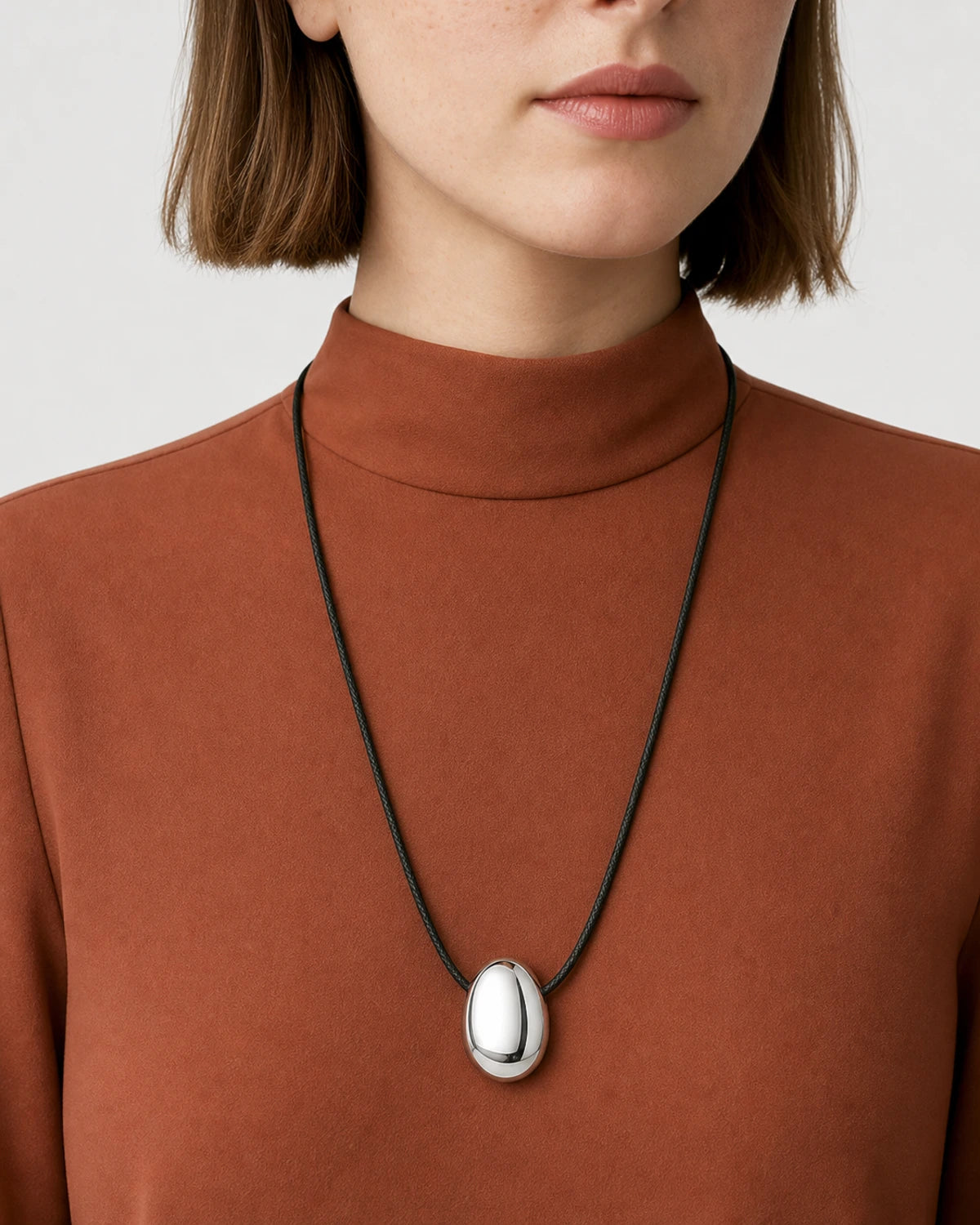 Mouth-down studio portrait wearing the Naiya silver pebble cord necklace
