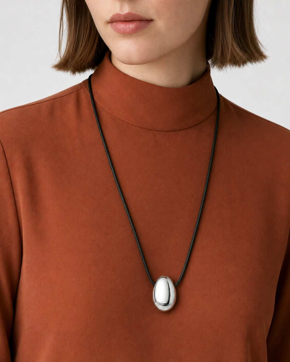 Clean mouth-down close-up wearing the Naiya silver pebble on black braided cord