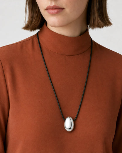 Clean mouth-down close-up wearing the Naiya silver pebble on black braided cord