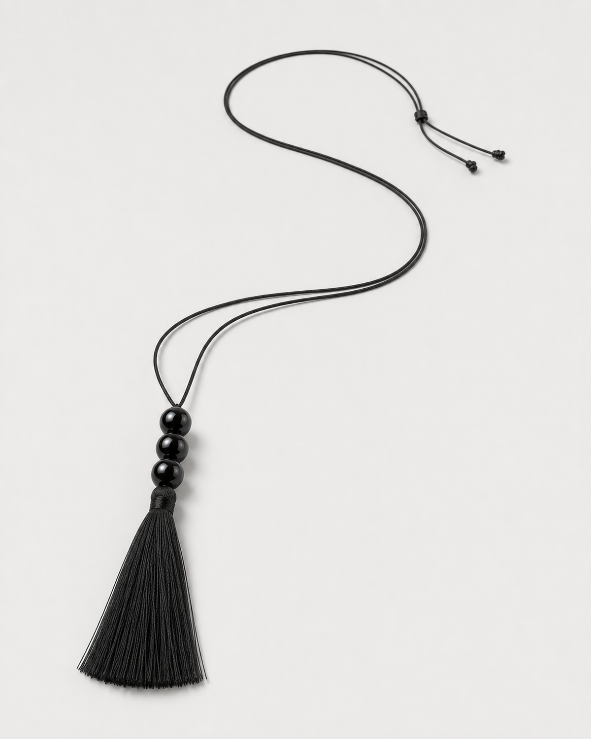 Alternate full-length view of the adjustable Nera black tassel necklace on pale dove-grey
