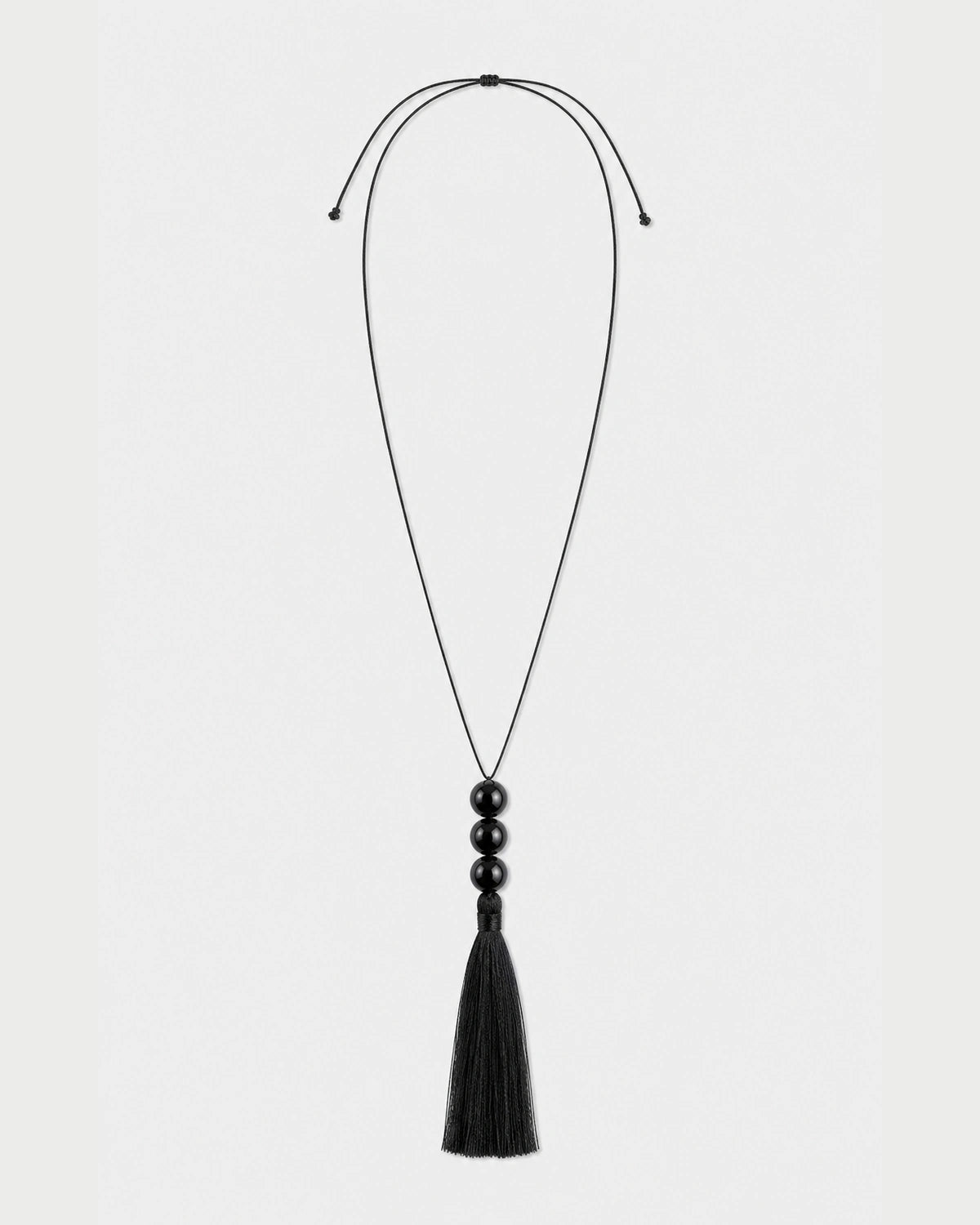 Nera black three-bead tassel necklace with adjustable cord on pale neutral grey