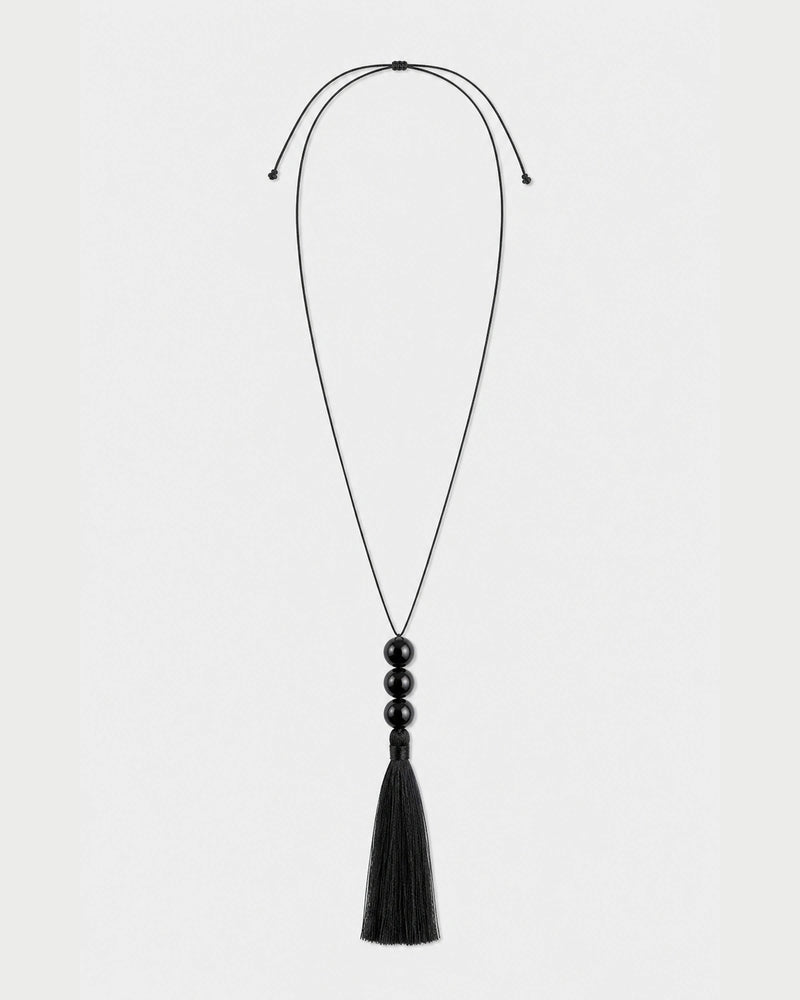 Nera black three-bead tassel necklace with adjustable cord on pale neutral grey