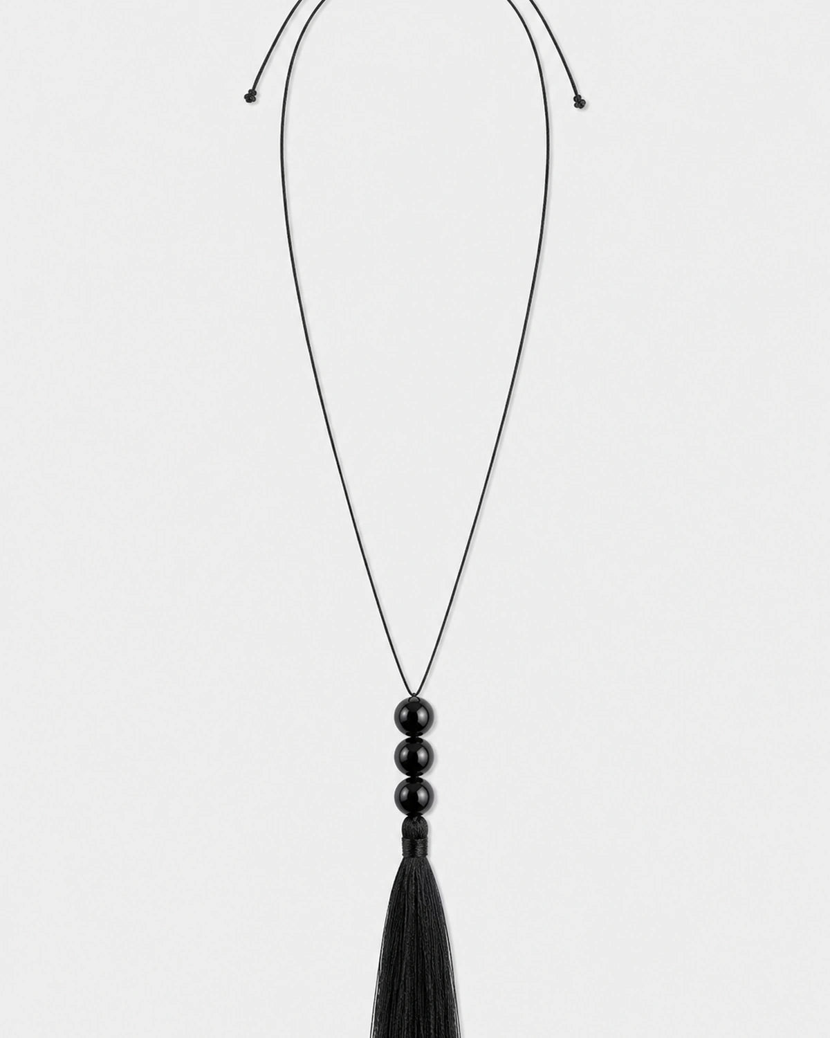 Nera black three-bead tassel necklace on a seamless pale dove-grey studio background