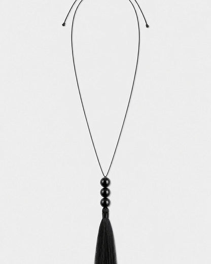 Nera black three-bead tassel necklace on a seamless pale dove-grey studio background