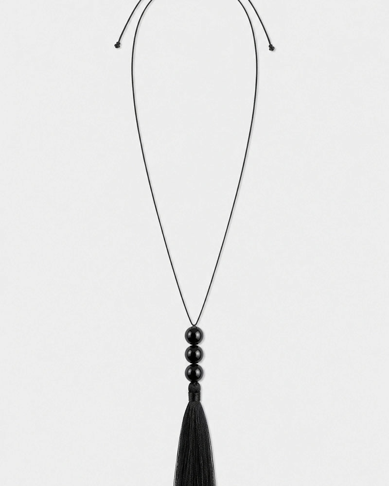 Nera black three-bead tassel necklace on a seamless pale dove-grey studio background