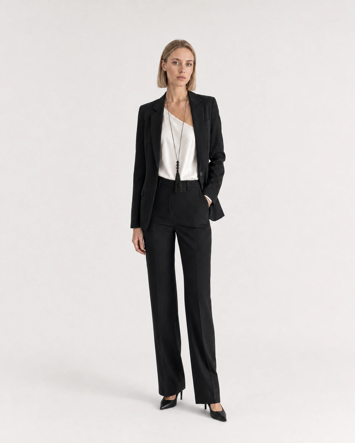 Wide studio portrait showing the Nera tassel necklace at natural scale with black tailoring