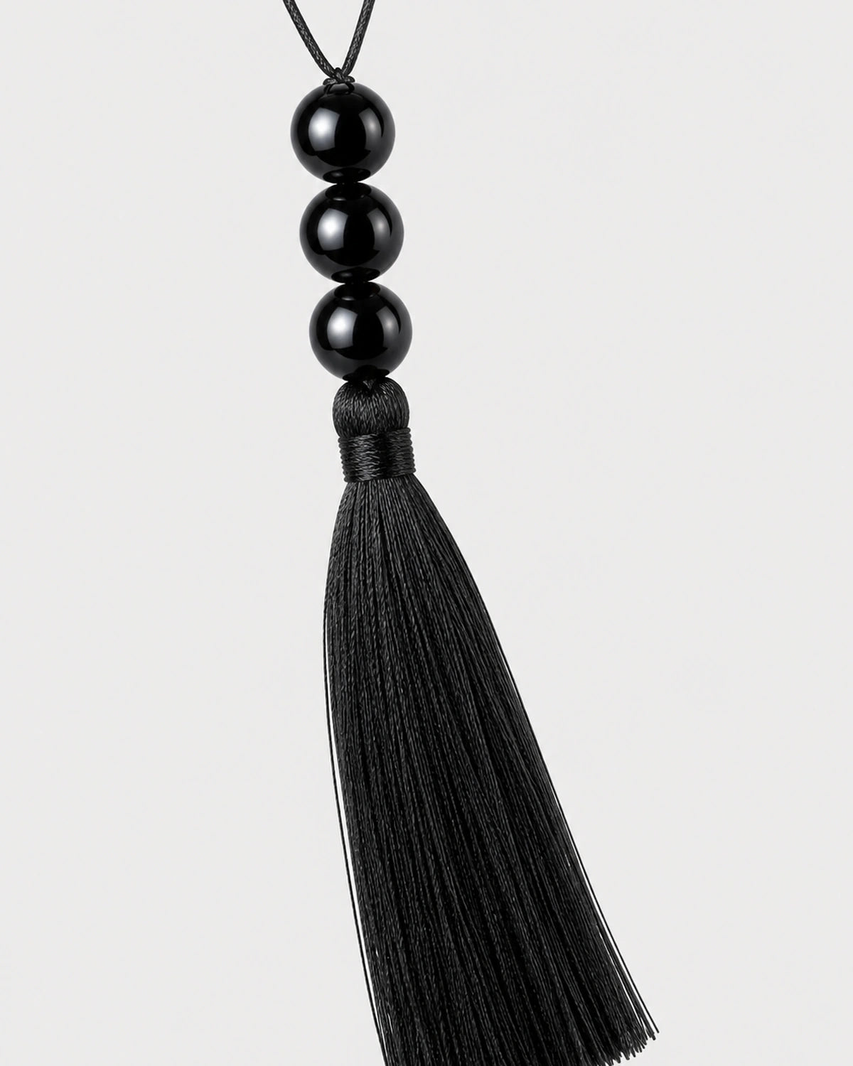 Macro detail of the Nera three glossy black beads and silk-look tassel