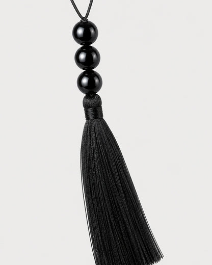 Macro detail of the Nera three glossy black beads and silk-look tassel