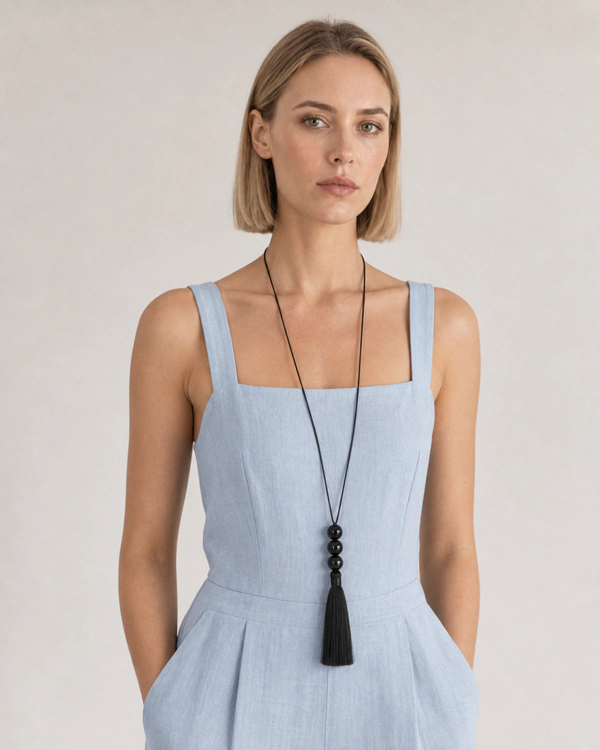 Model in a powder-blue linen jumpsuit wearing the long Nera tassel necklace