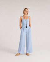 Wide studio portrait in a blue linen jumpsuit featuring the Nera tassel necklace