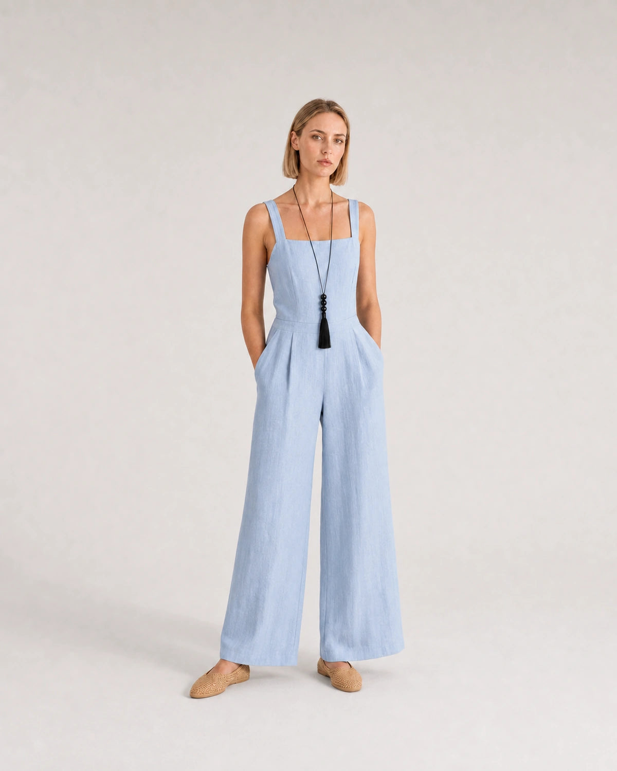 Wide studio portrait in a blue linen jumpsuit featuring the Nera tassel necklace