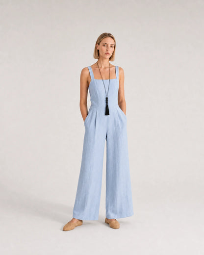Wide studio portrait in a blue linen jumpsuit featuring the Nera tassel necklace