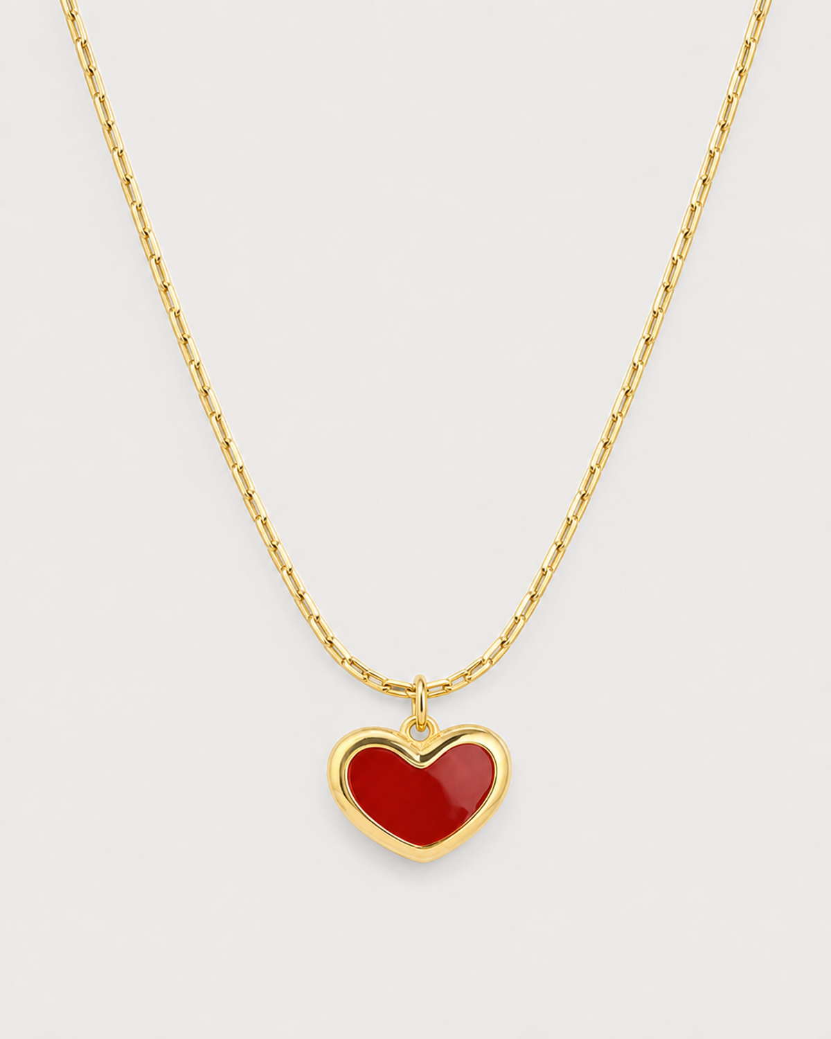 Macro of the Noemie glossy crimson heart, raised gold rim and fine bar-link chain