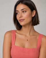 Model in coral linen wearing the Noemie gold crimson heart necklace
