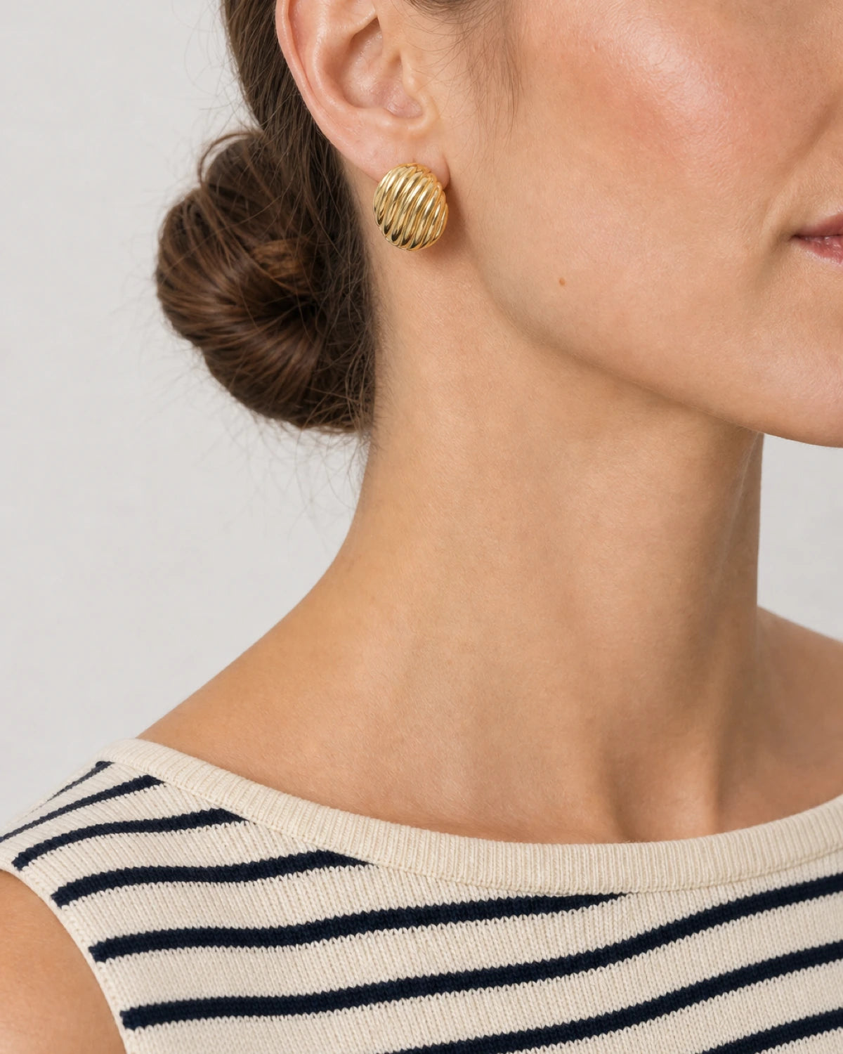 Eye-free right profile of Claudia wearing the gold Odette ribbed oval stud