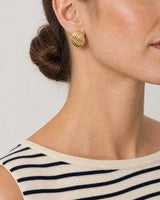 Eye-free right profile of Claudia wearing the gold Odette ribbed oval stud